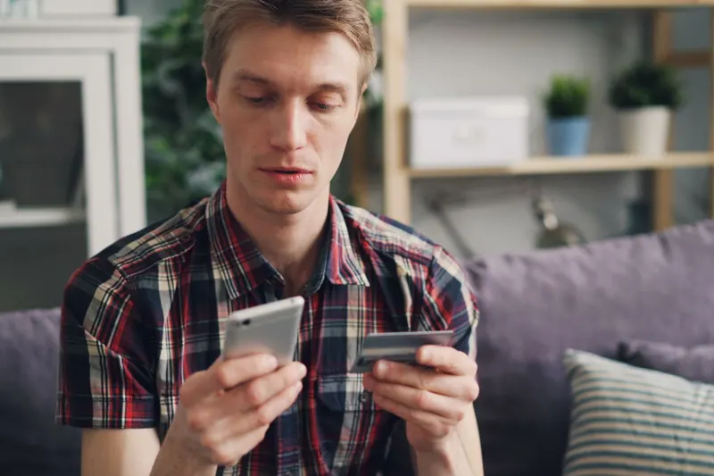 Jongeman op de bank met smartphone en betaalpas