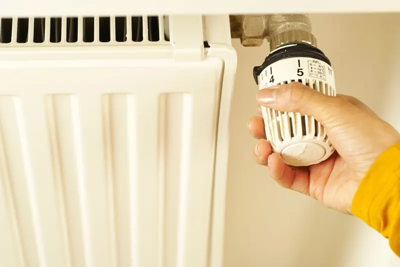 Hand draait aan de thermostaatknop van een radiator